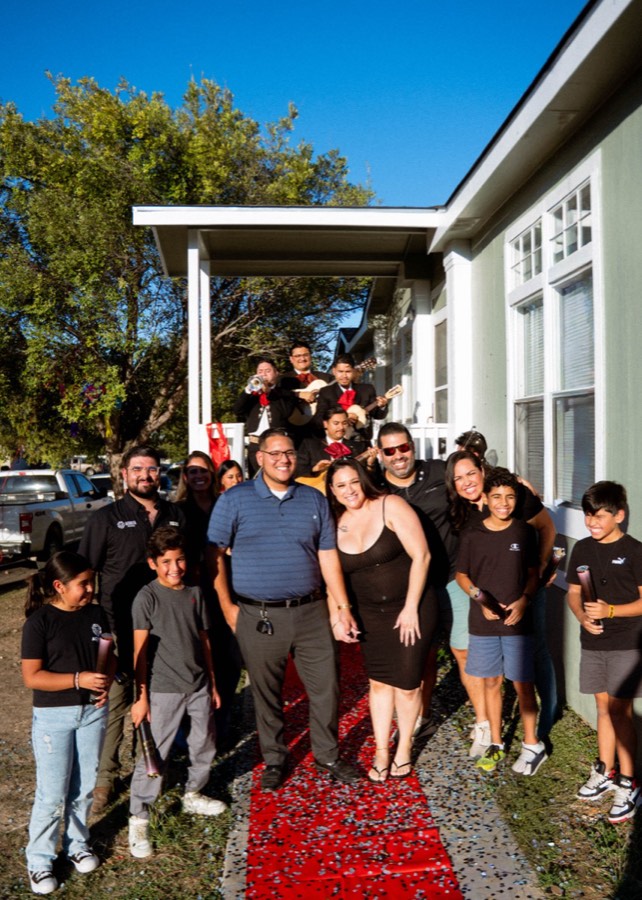 An Acosta family and their kids celebrating on the red carpet with mariachis playing on the porch of their new home
